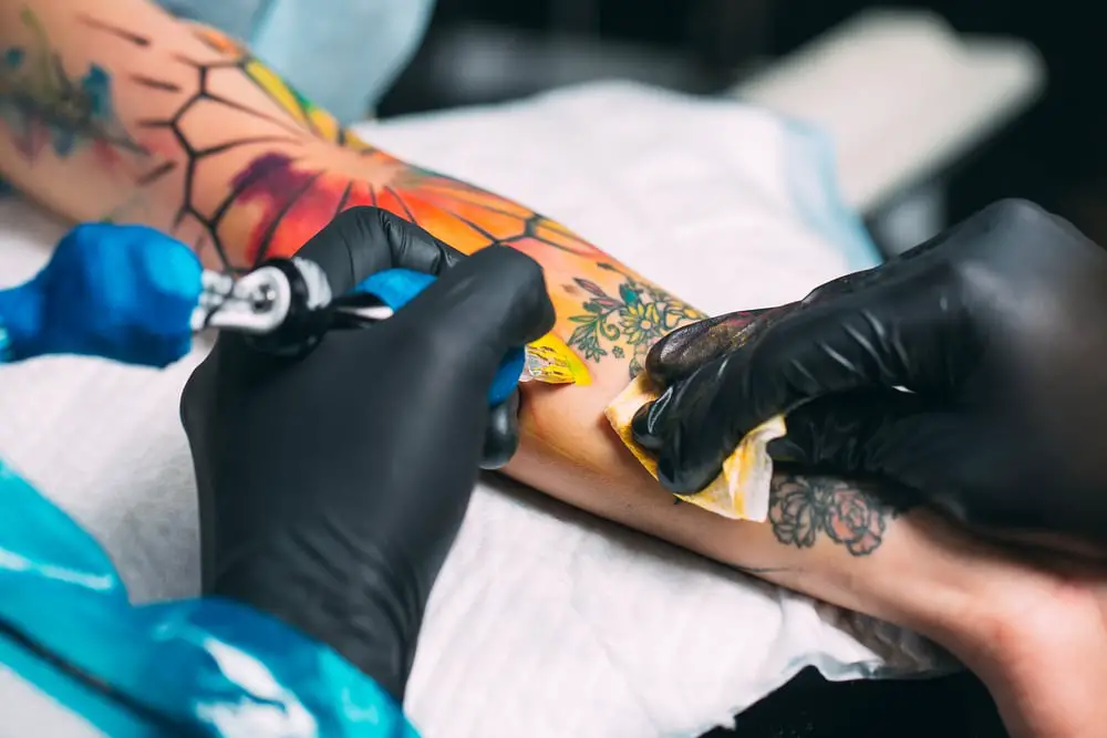 tattoo artist tattooing a colourful forearm tattoo