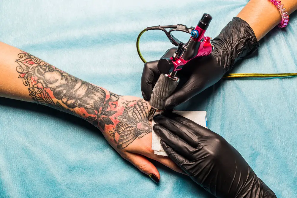 tattoo artist putting a tattoo on a womens hand