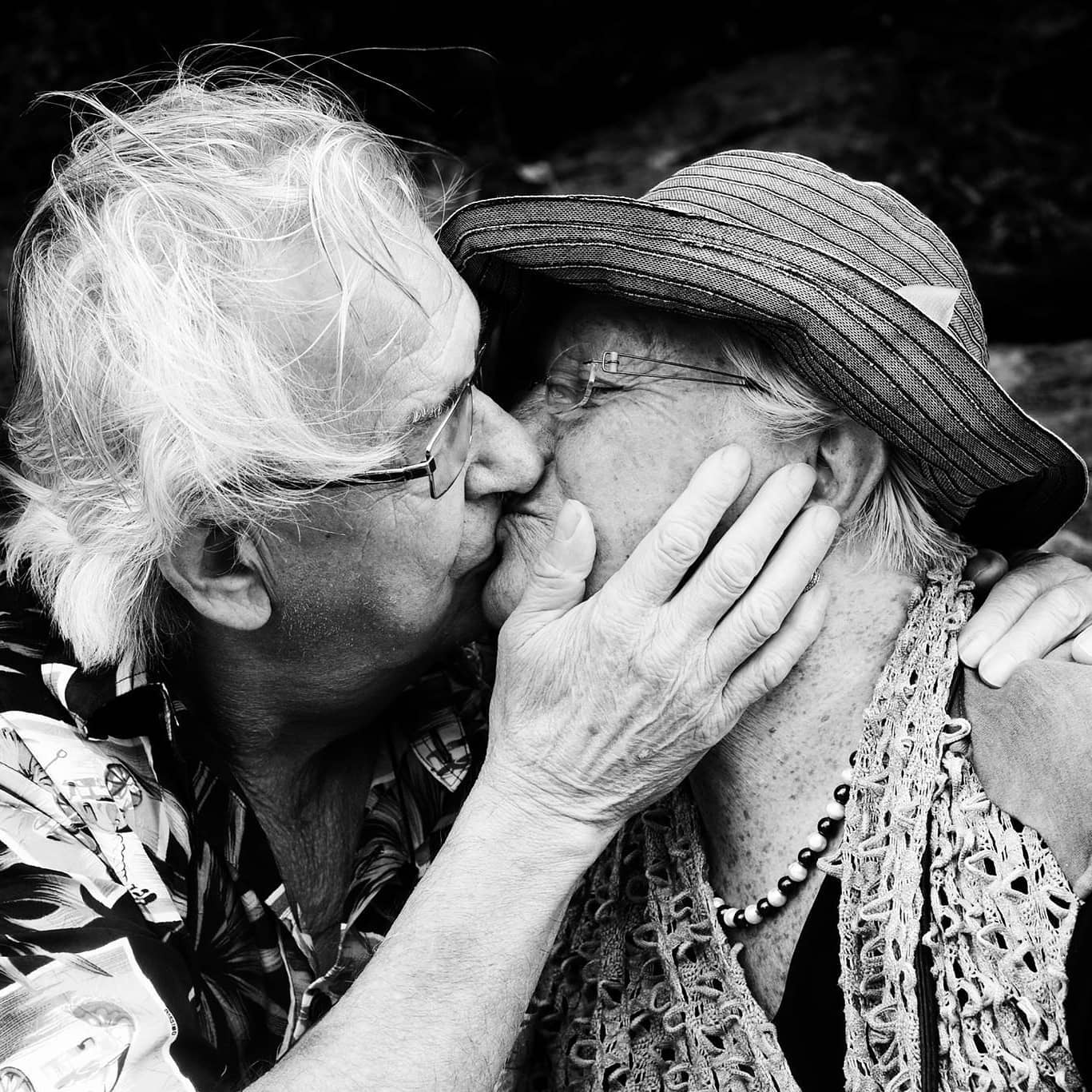 a black and white picture of an old couple kissing