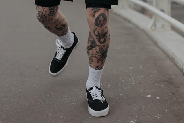 male with leg colorful tattoos walking in the street