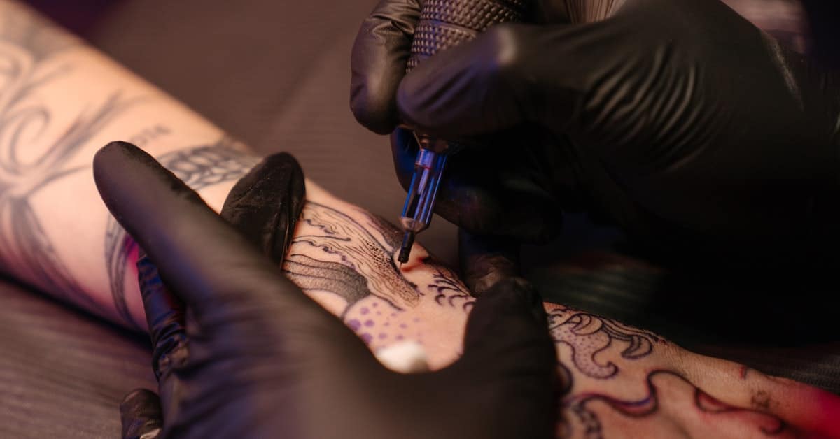 tattoo artist performing a black tattoo on a mans forearm.