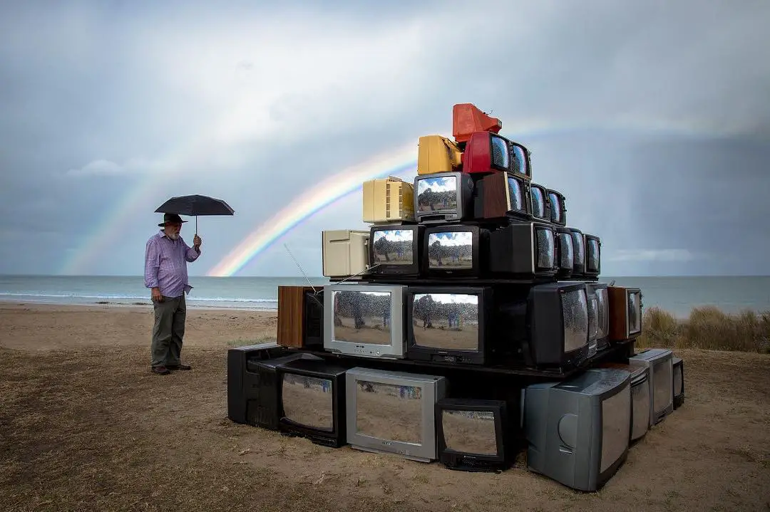 a television art installation with an old man and double rainbow background