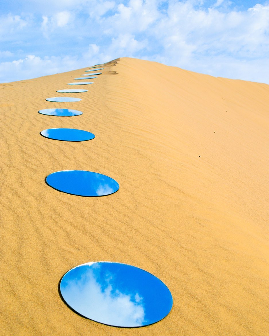 circular mirrors lined up in the vast desert reflecting the blue sky