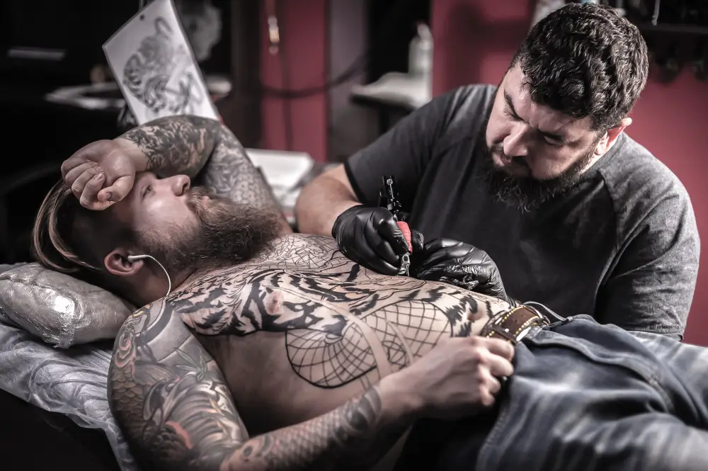 tattoo artist wirking on man with full body black tattoos