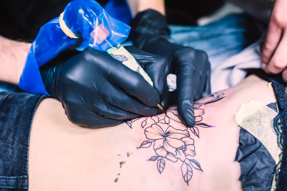 tattoo artit drawing fine flowers on a womens side