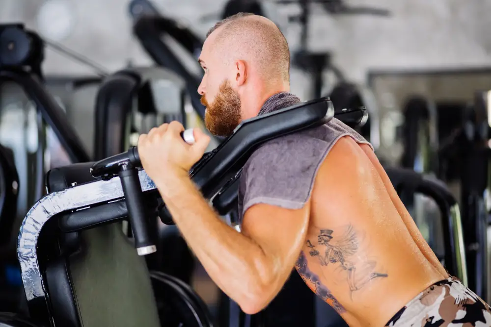 strong bald man training in the gym with no shirt and large black side tattoos