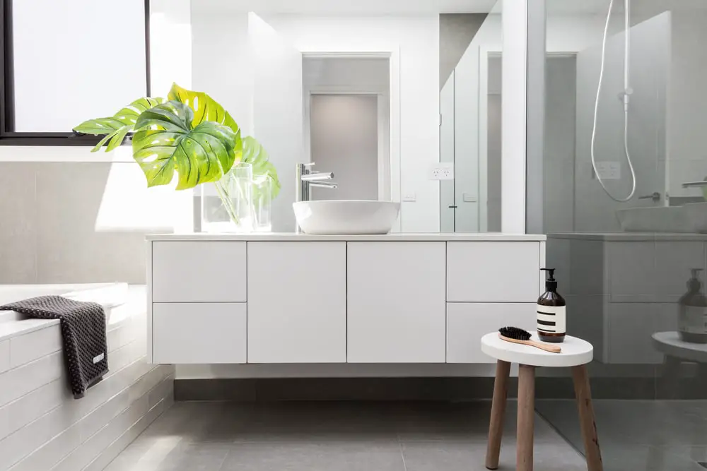 minimalist white bathroom design with accents of forest green philodendron leaves on a clear glass vase with accents of dark brown palettes 