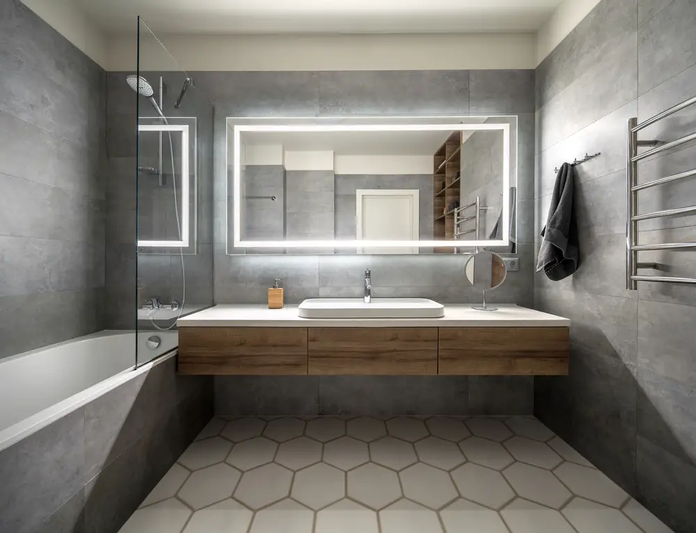 gray bathroom design with gray wall tiles, dark wooden wall mounted storage space and drop in lavatory and large rectangular mirror
