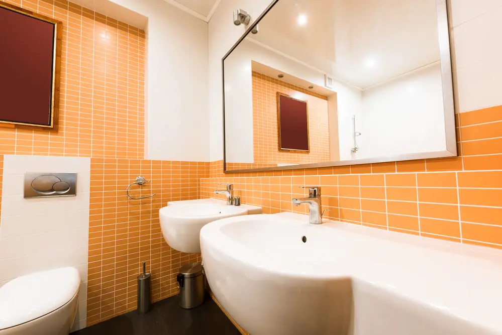 copper orange wall tiles with rectangular large mirror accentuated with chrome finished bathroom fixtures