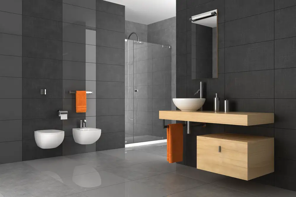a slick dark gray modern bathroom design with light colored wood veneer wall mounted white acrylic lavatory with accents of bright orange