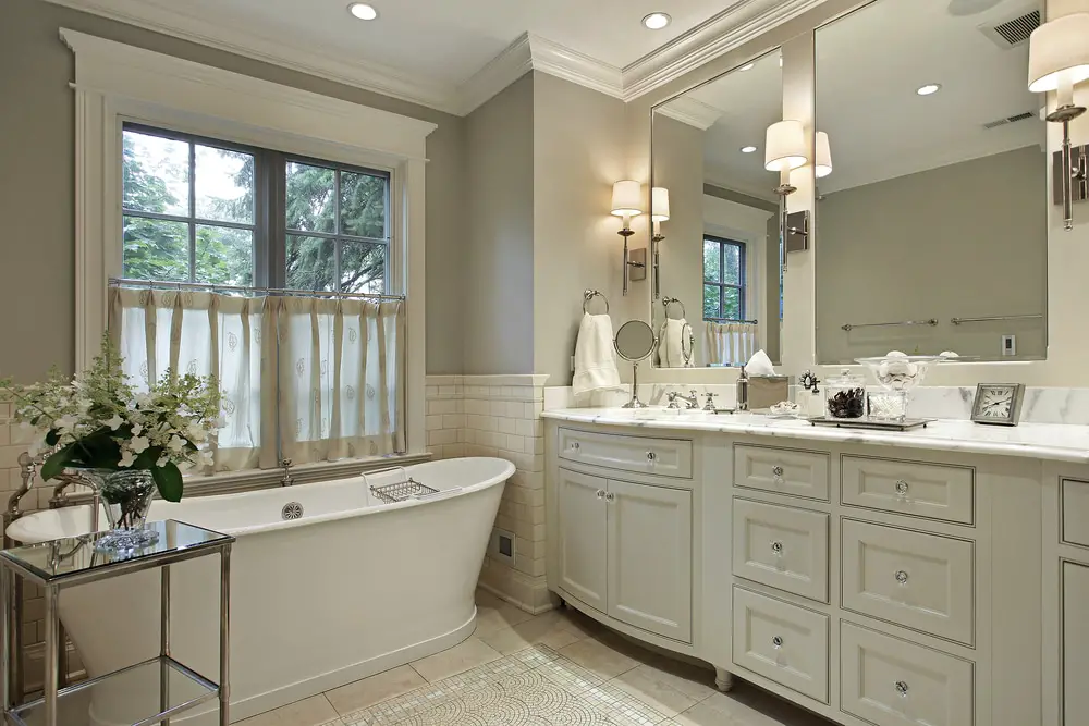 ceramic white bathroom design with light gray walls paneled storage cabinets freestanding white acrylic tub and double french window