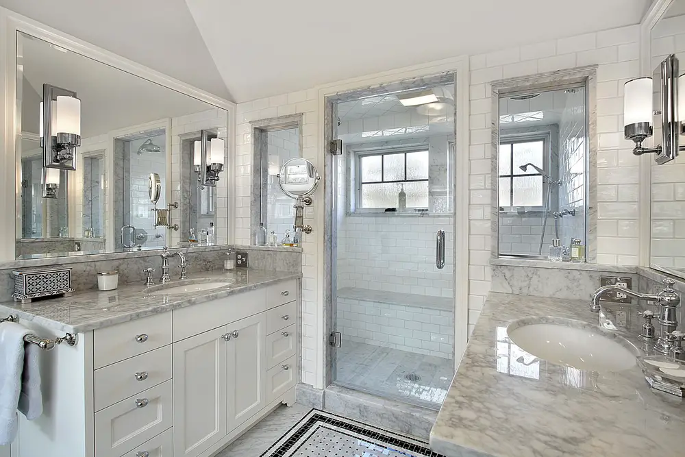 ceramic white bathroom design with white and gray marble countertop chrome finished bathroom fixtures and bluish gray glass shower door