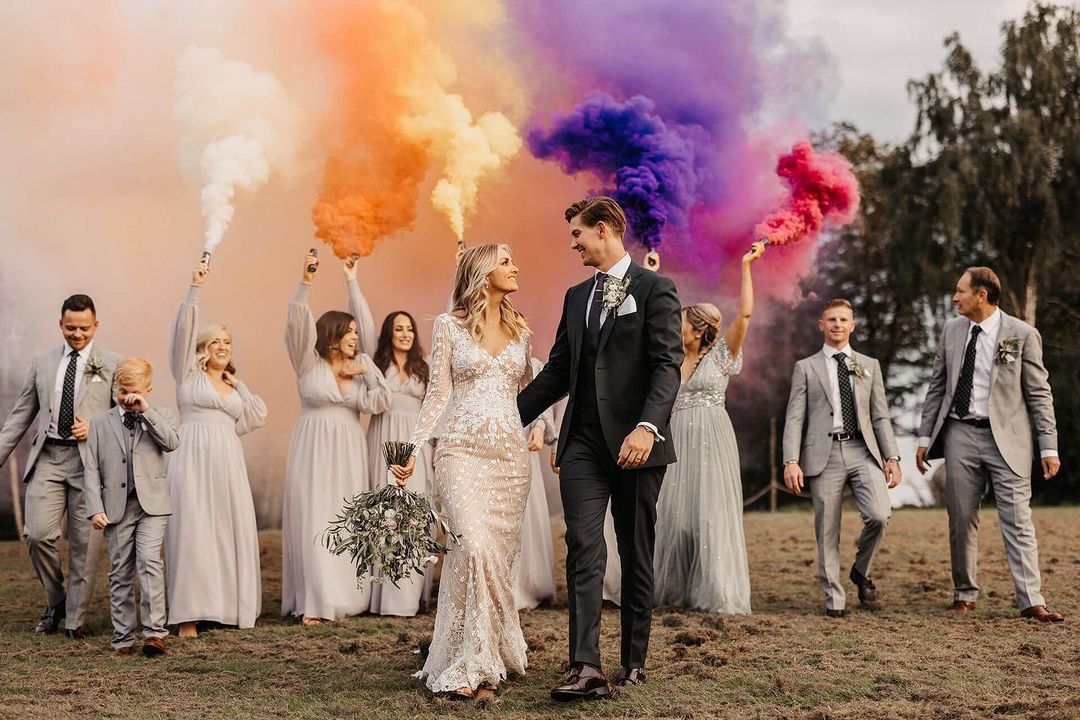 a picture of the newlywed couple with colorful powder blown on the background by wedding guests