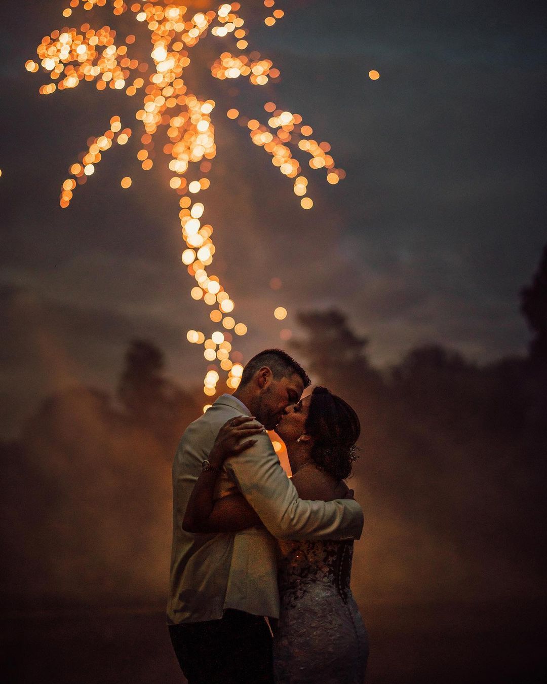 a picture of a couple kissing with fireworks on the background