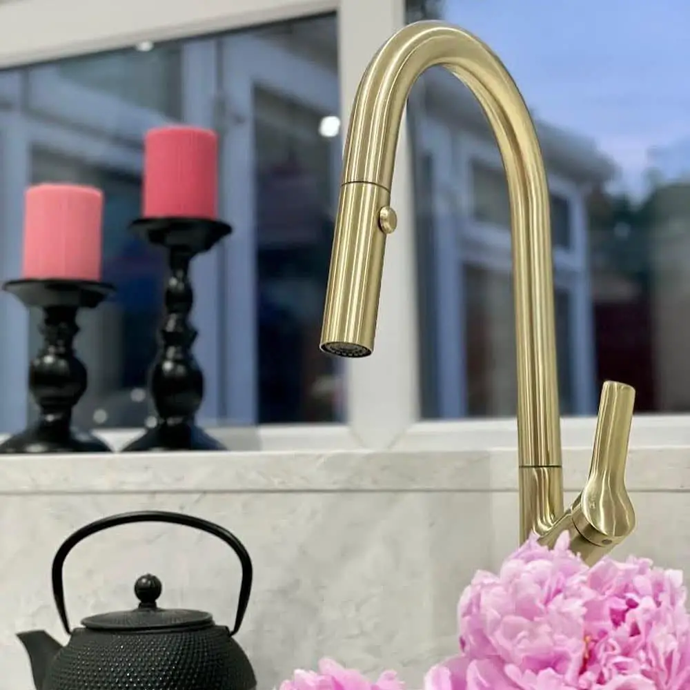 a polished gold kitchen faucet on a gray marble kitchen countertop decorated with gothic candlesticks and lilac carnation