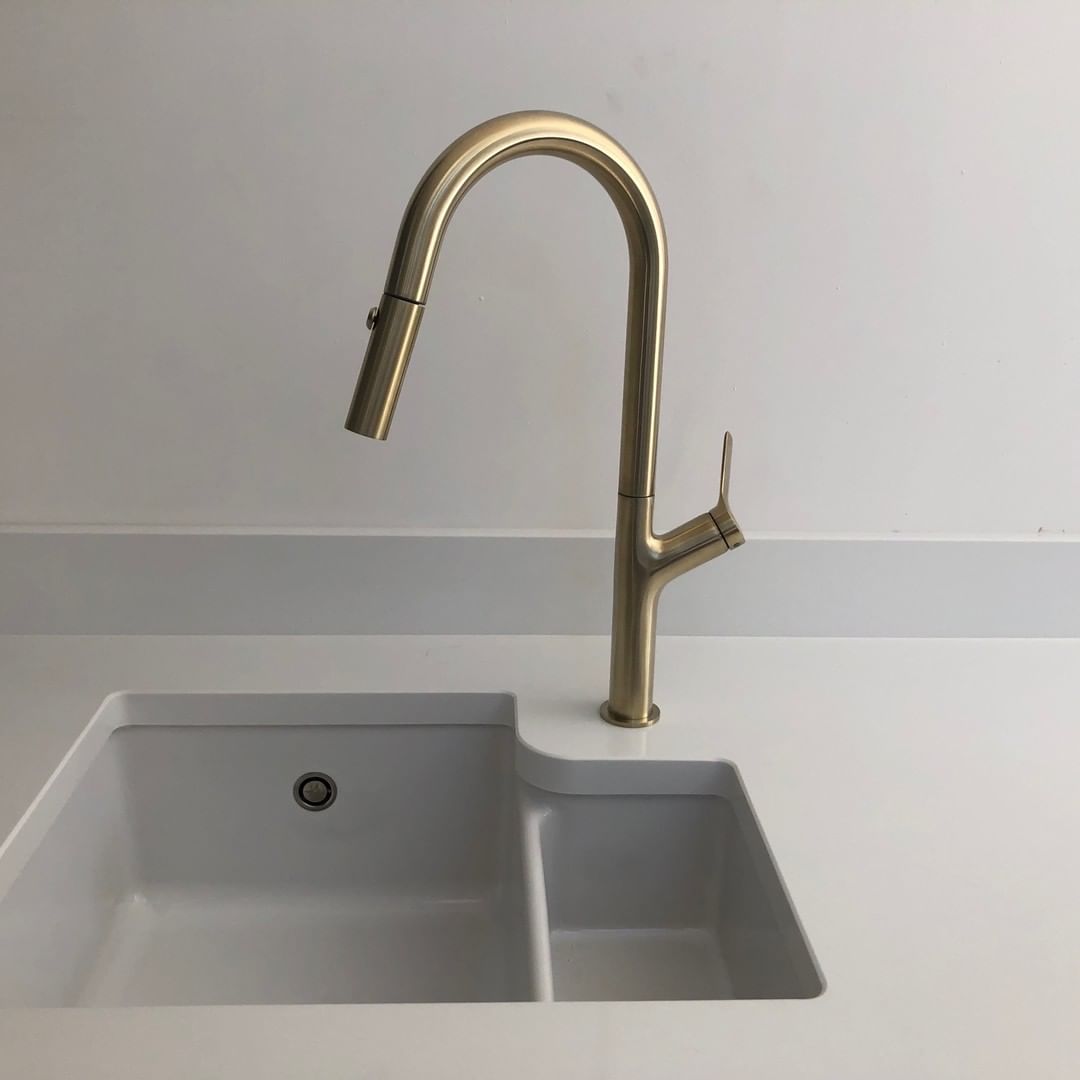 a sleek brass kitchen faucet on a white kitchen wall and countertop