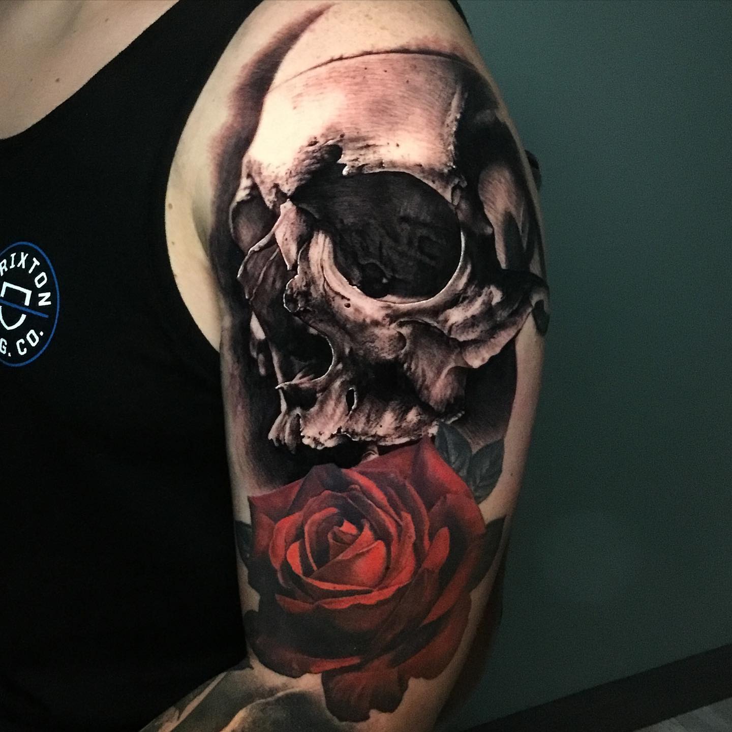 a skull and red rose tattoo on a mans arms