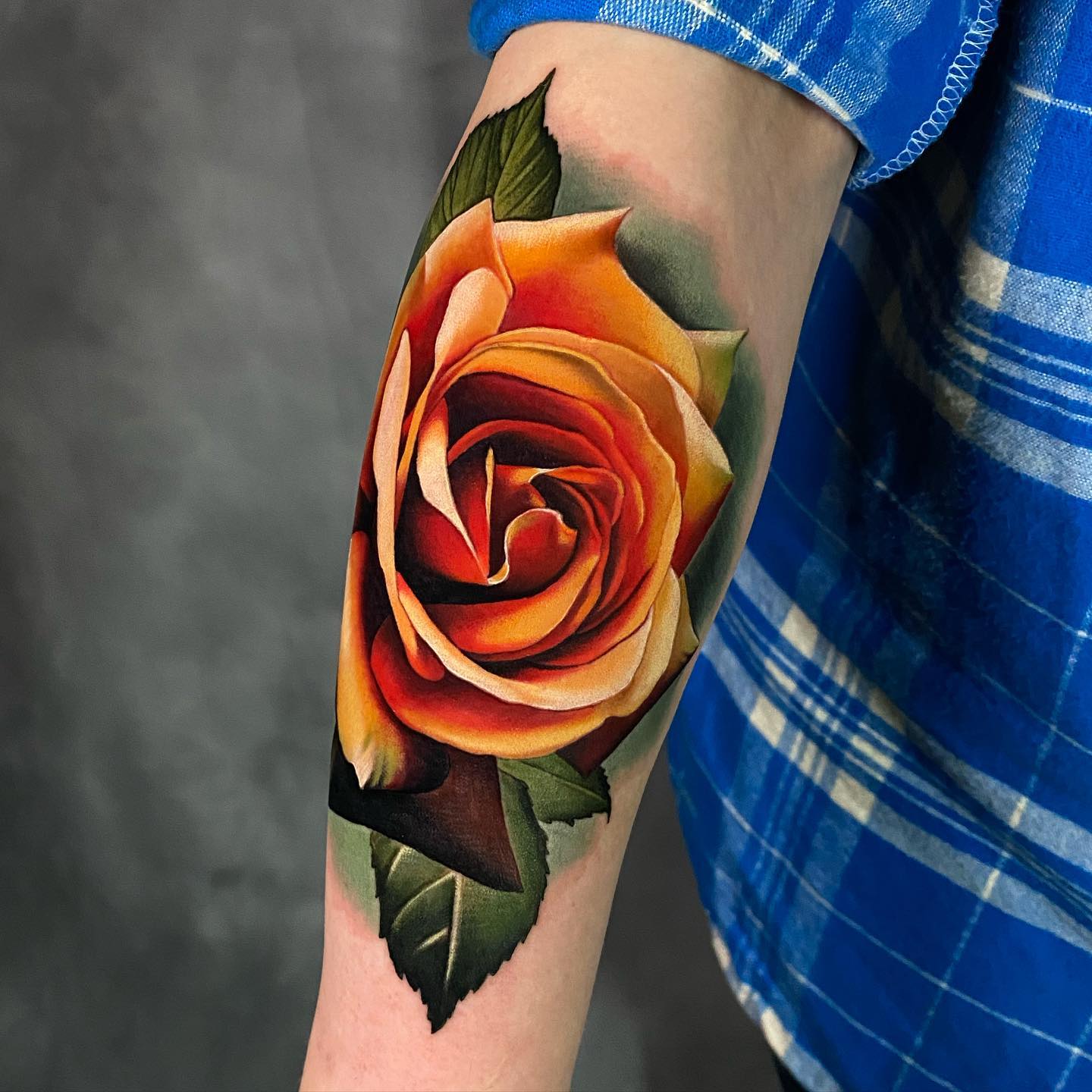 bright orange single rose tattoo on mans forearm